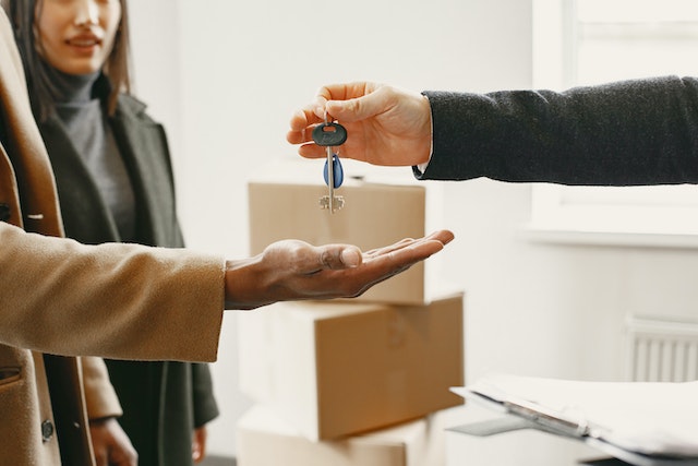 Person passing house keys to two tenants with moving boxes in the background